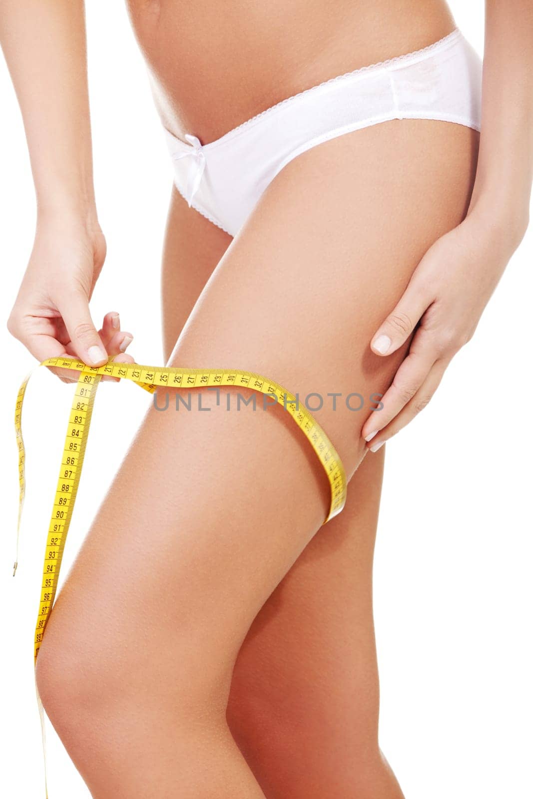 Closeup photo of a Caucasian woman's leg. She is measuring her thigh with a yellow metric tape measure after a diet