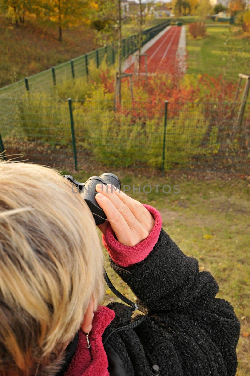 Mature woman looks through binoculars at the edge of the forest