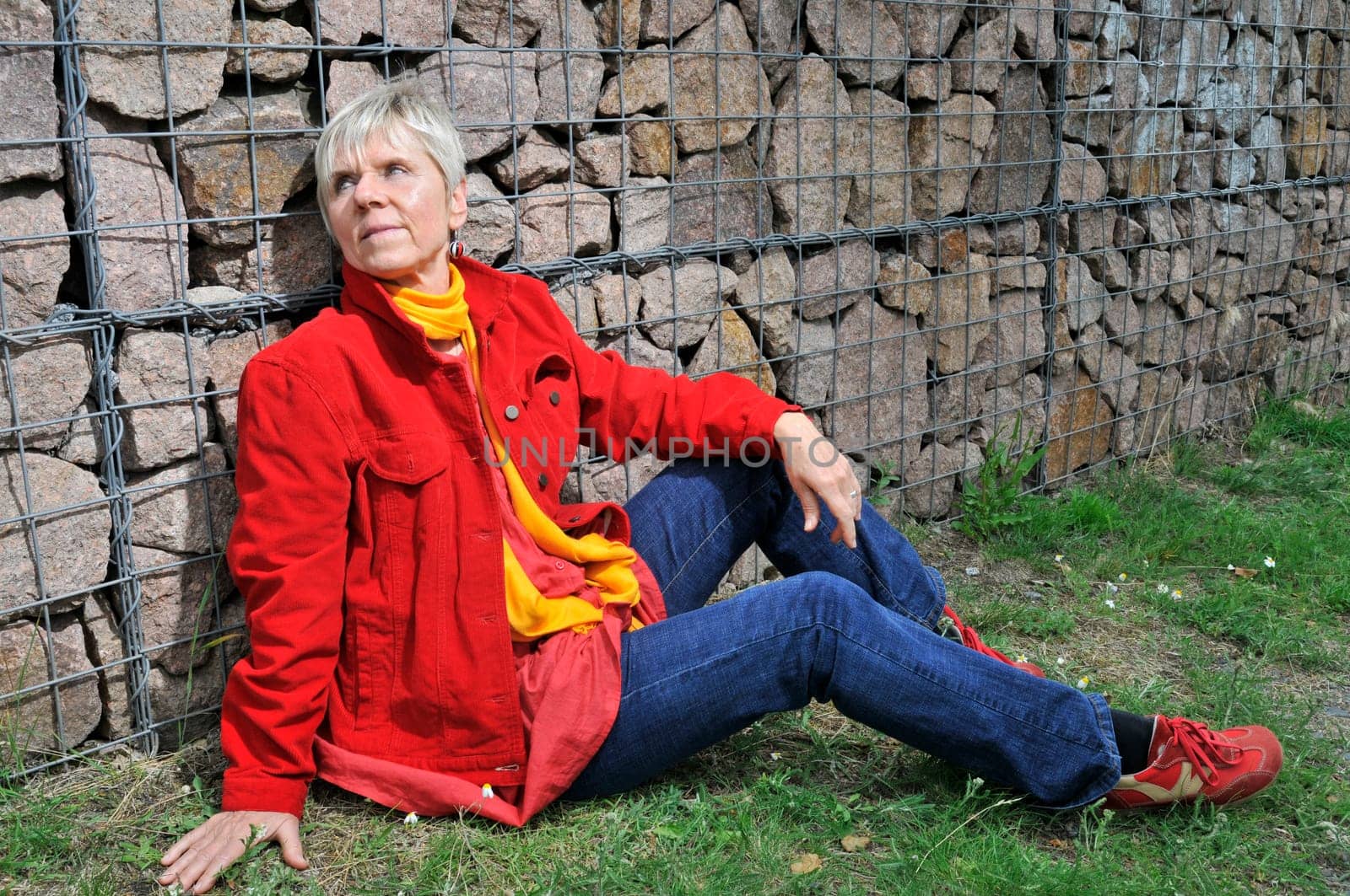 elderly woman with a red jacket sits on a stone wall  Mature woman in red jacket sitting at the stone wall