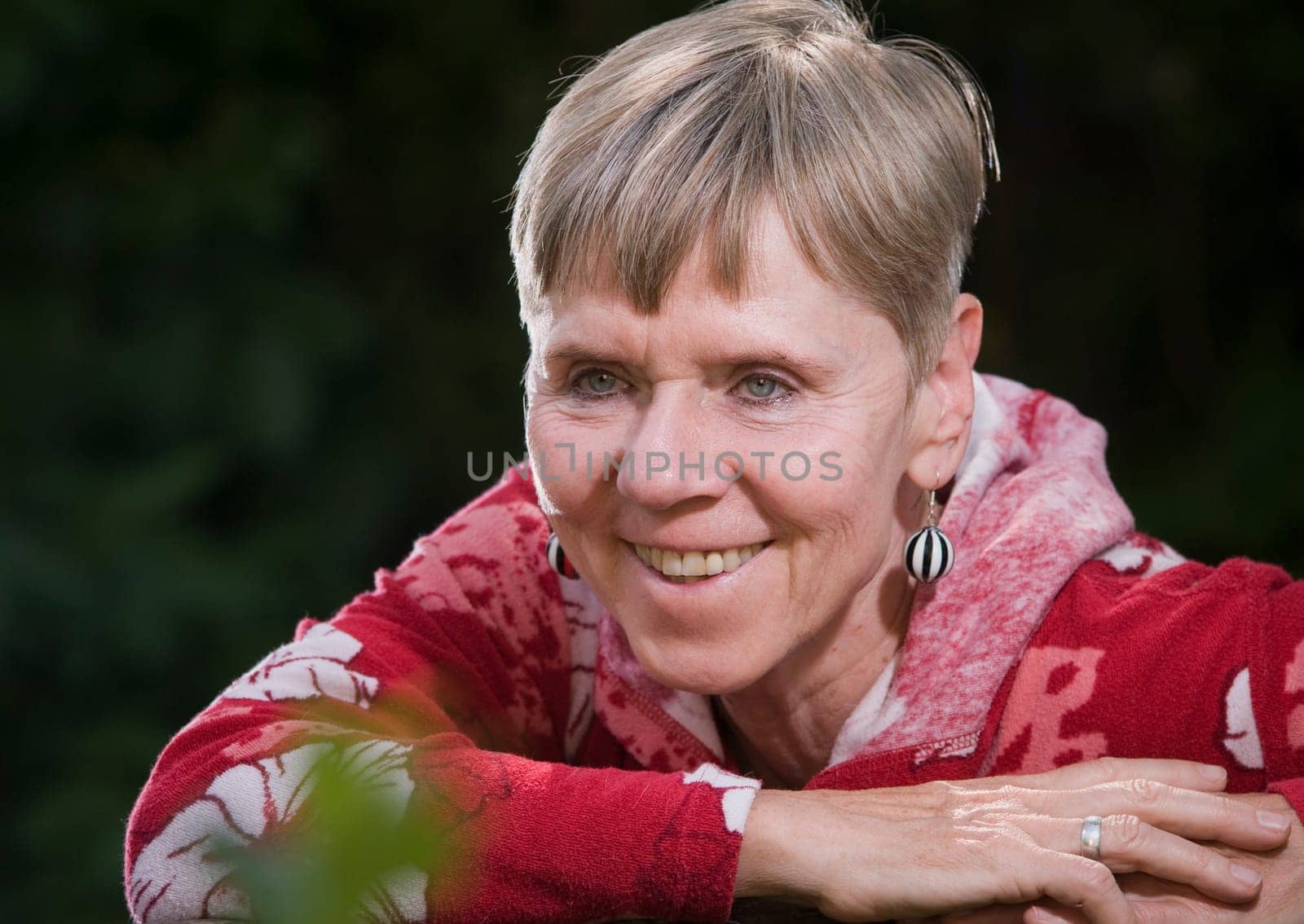 Portrait of an elderly woman on a park bench in summer with her upper body turned backwards over her backrest towards the camera