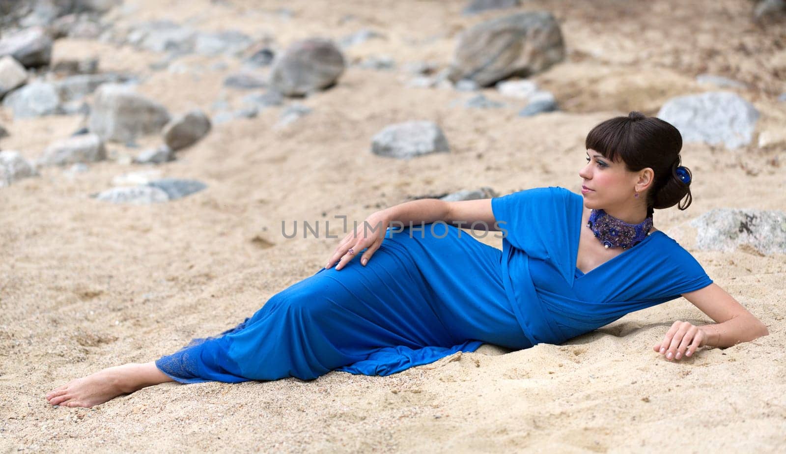 girl in a blue dress lying on the sand
