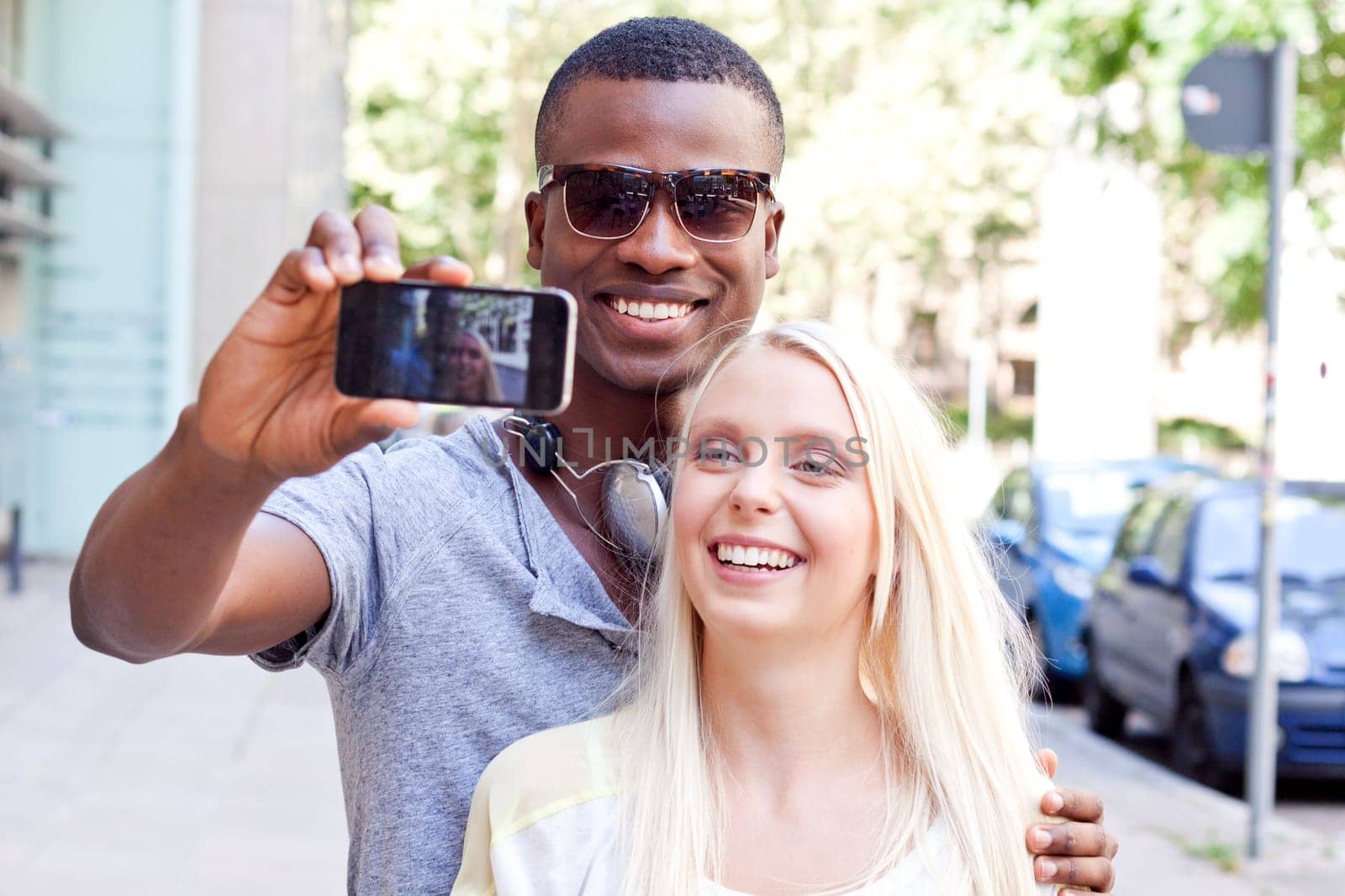 Young laughing multicultural couple take photo with smartphone mobile phone in summer
