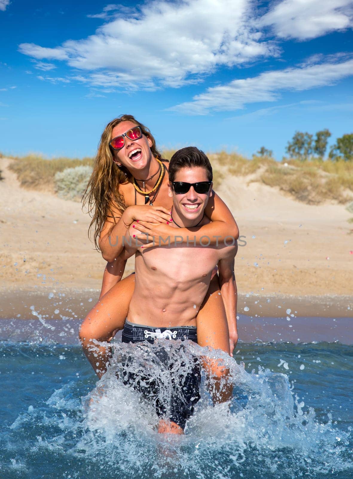 Teen couple enjoying  piggyback on summer beach shore splashing water