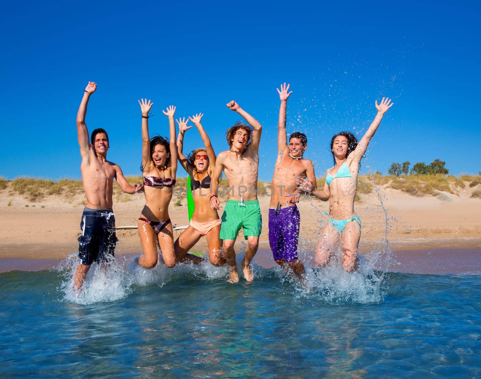 Happy excited teen boys and girls group jumping at the beach splashing water