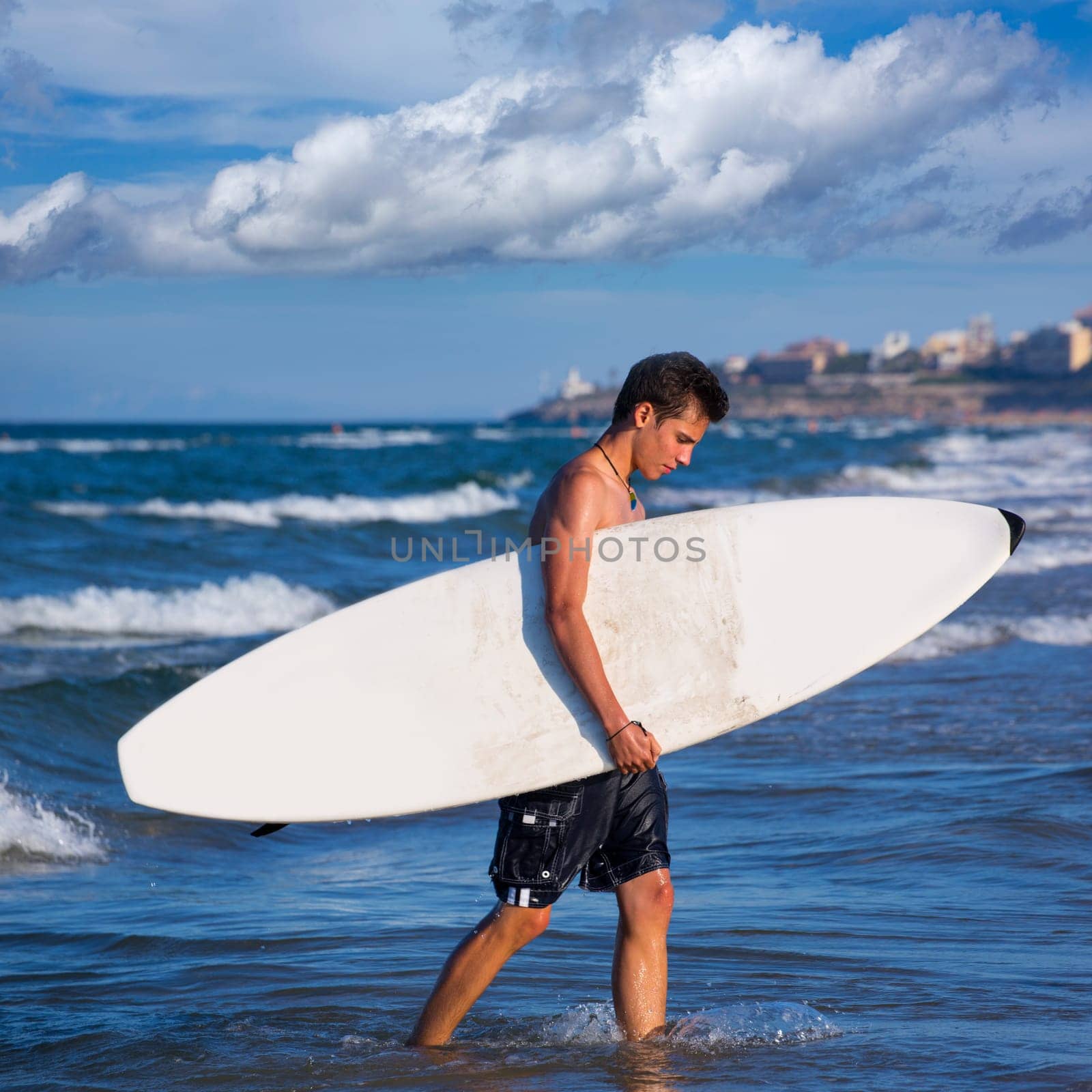 boy handsome surfer holding surfboard coming out from the waves