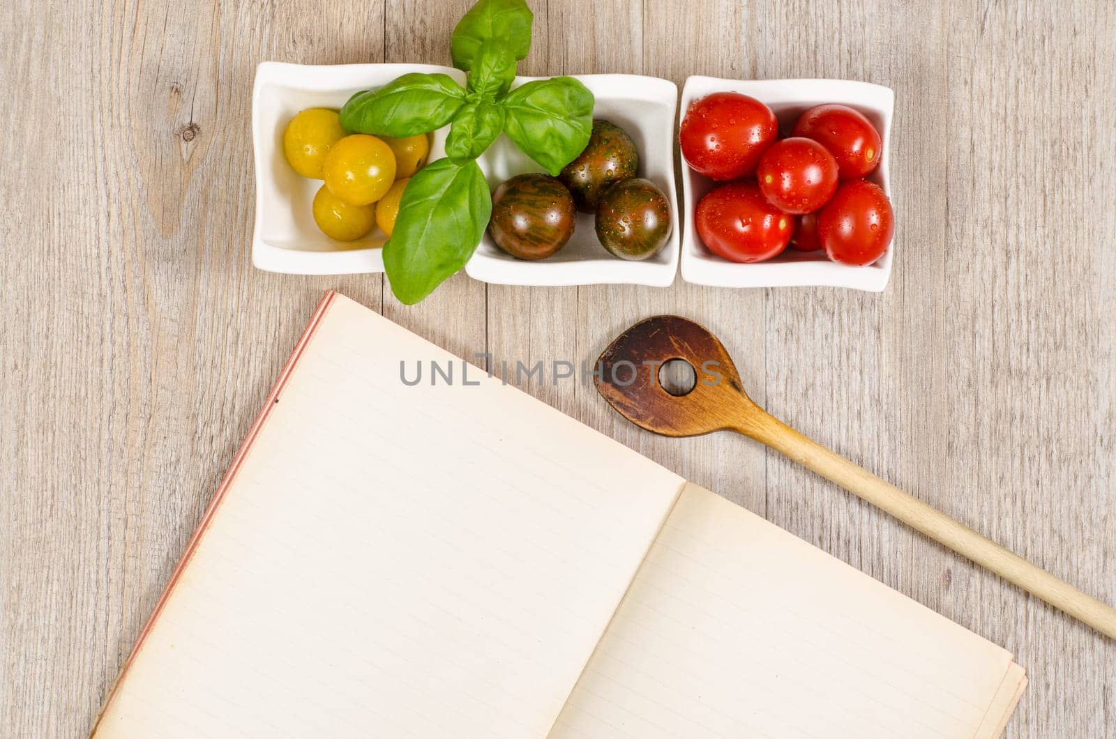 Blank paper from a book and a wooden wooden spoon with tomatoes and basil