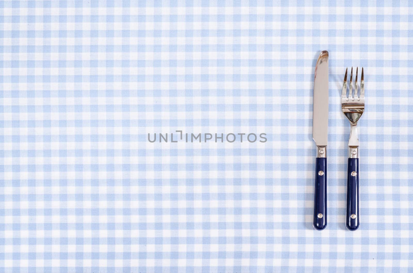 Knife and fork in blue checkered on tablecloth and text space