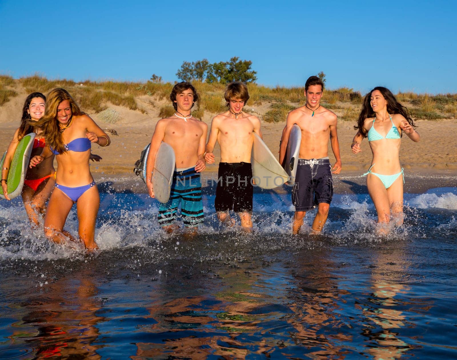 surfer teenagers boys and girls group running happy to the beach splashing water