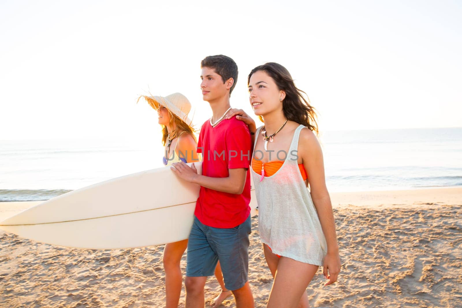 Surfer girls with teen boy walking on beach shore high key