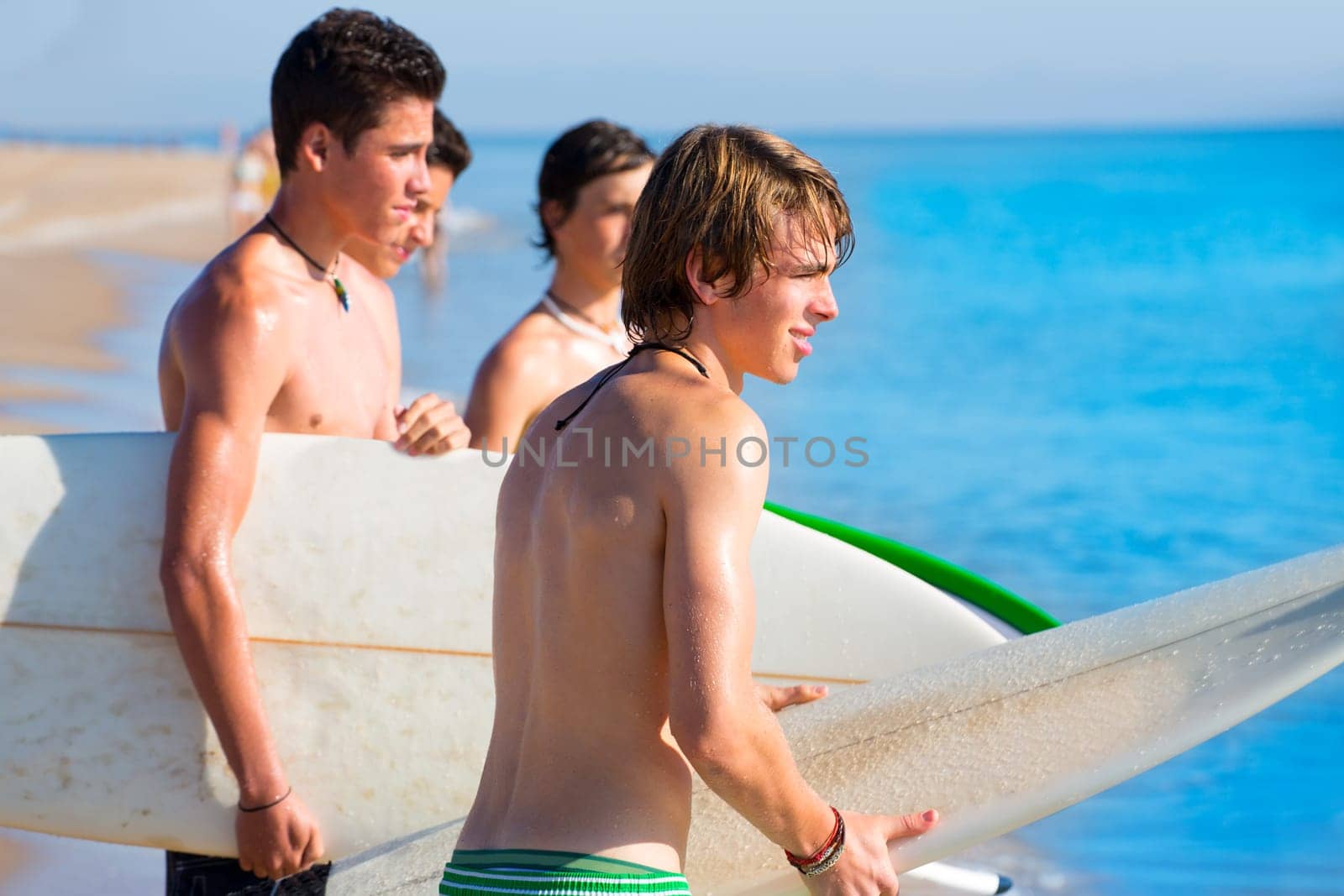 Surfer teen boys talking on beach shore holding surfboards