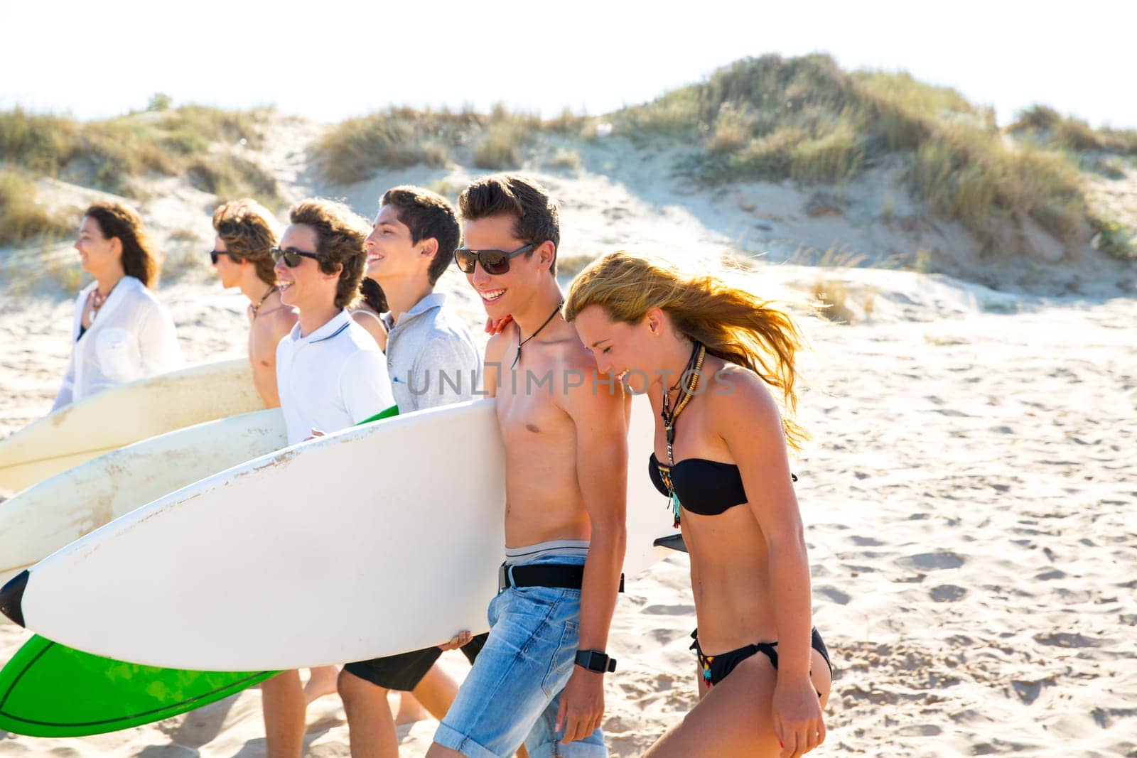 Surfer teen boys and girls group walking on beach sand