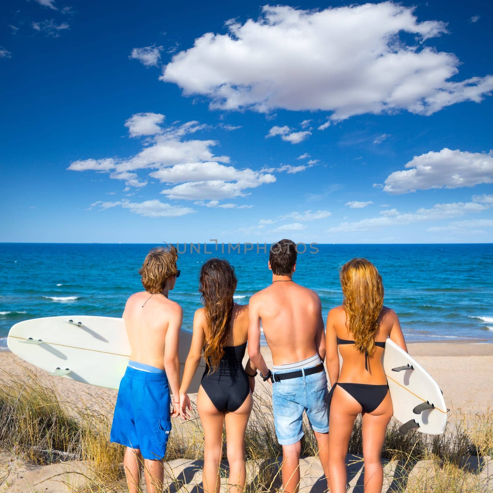 Boys and girls teen surfers rear back view looking at beach from uo dune