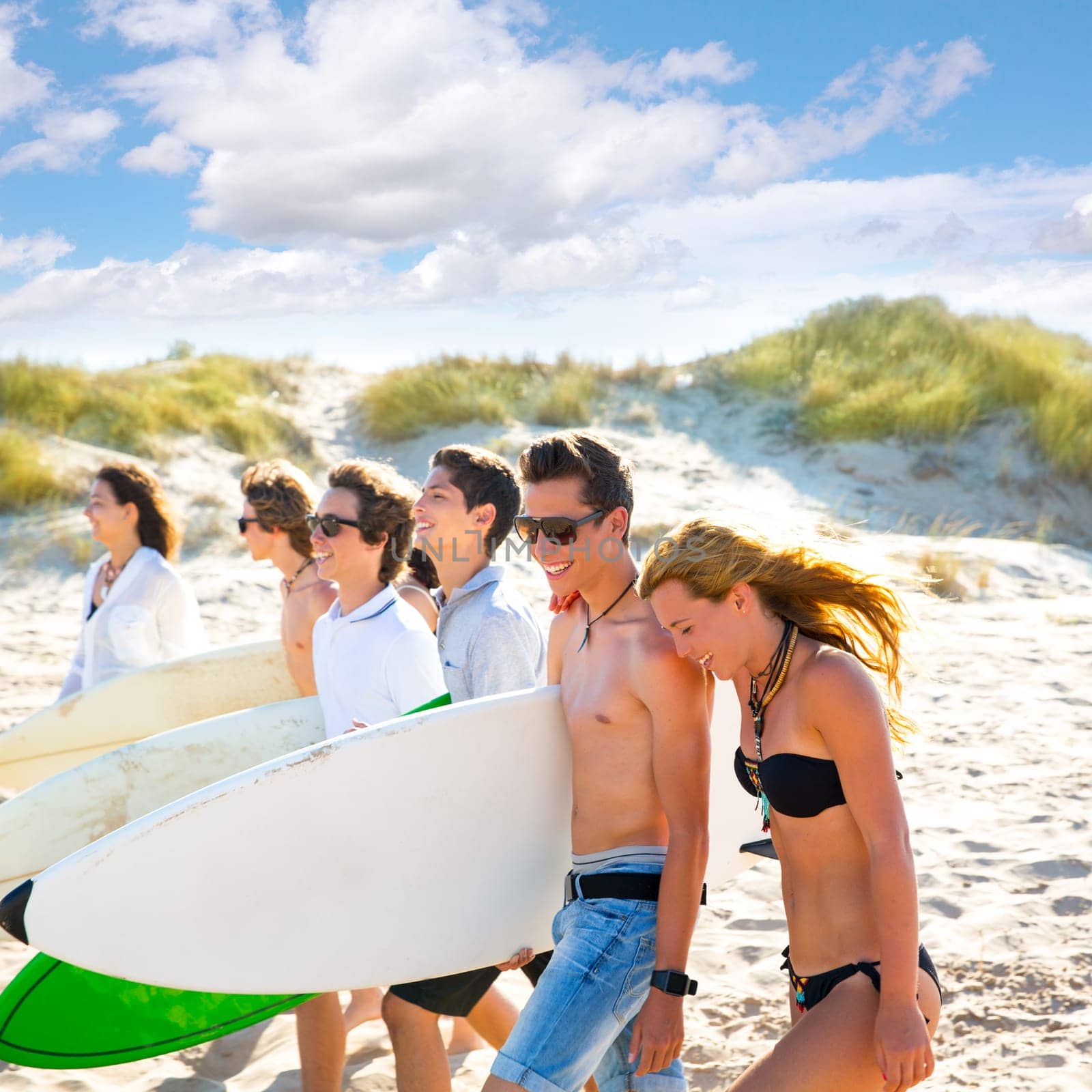 Surfer teen boys and girls group walking on beach sand