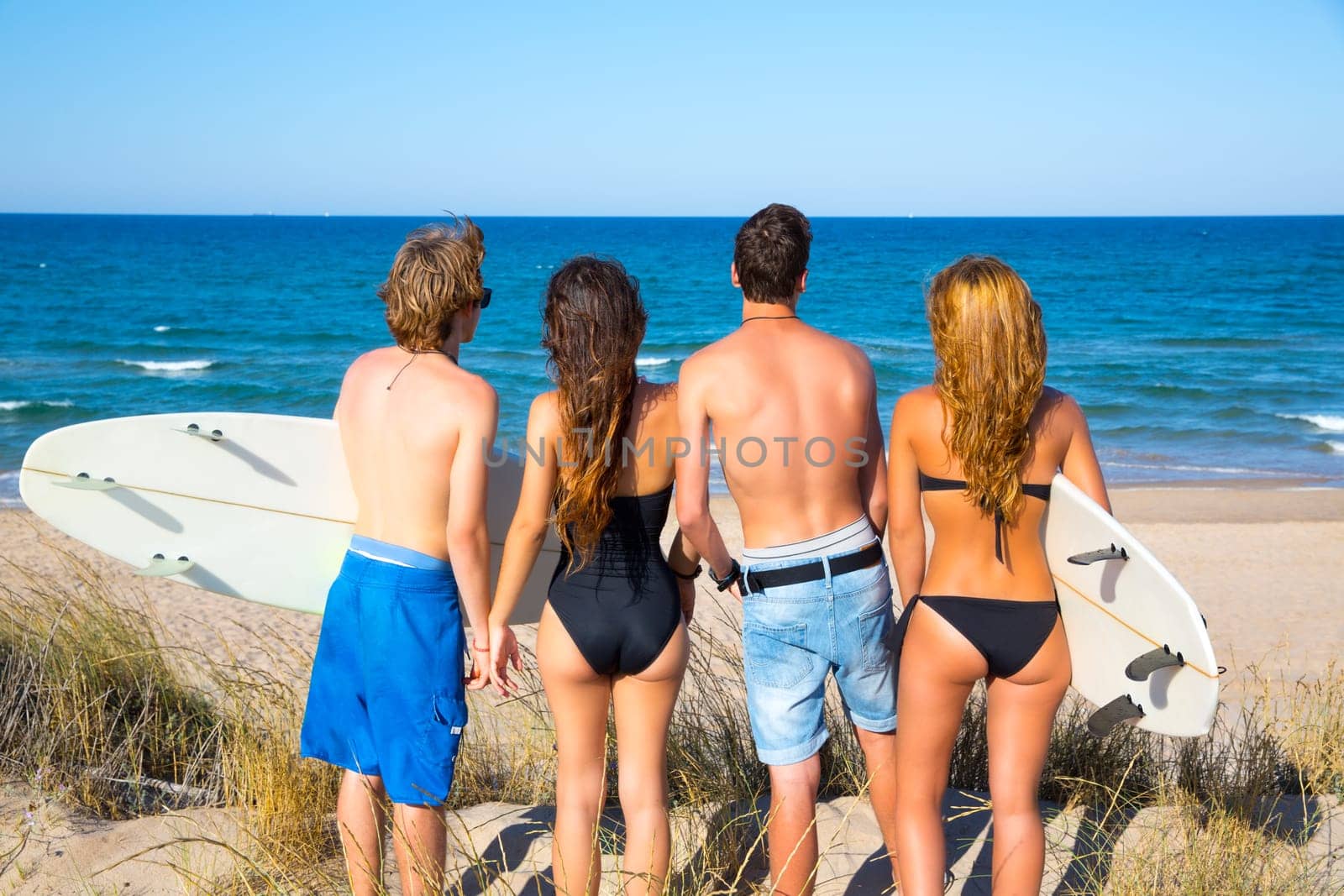 Boys and girls teen surfers rear back view looking at beach from uo dune