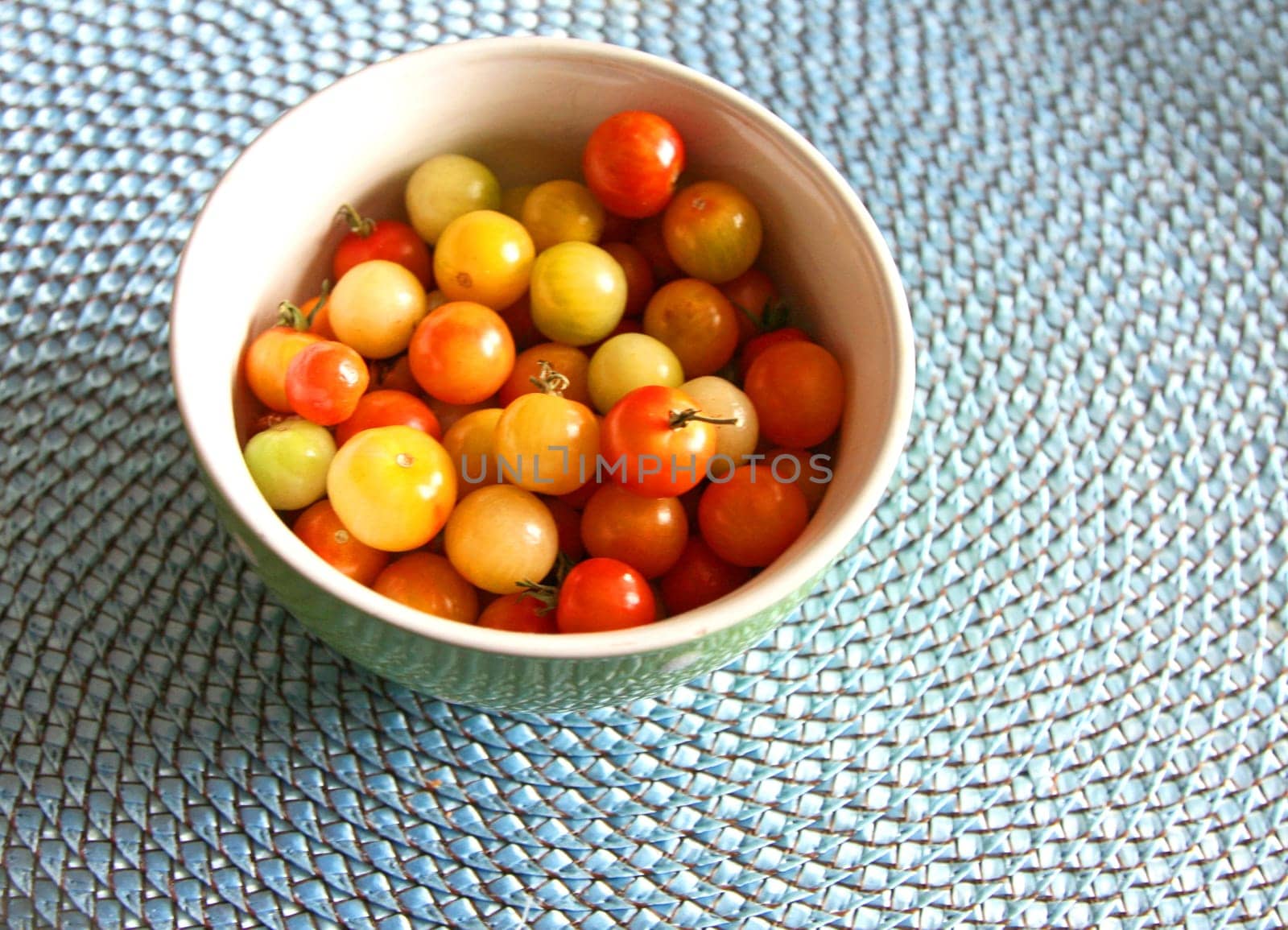 Multi-colored cherry tomatoes in a bowl on a blue mat