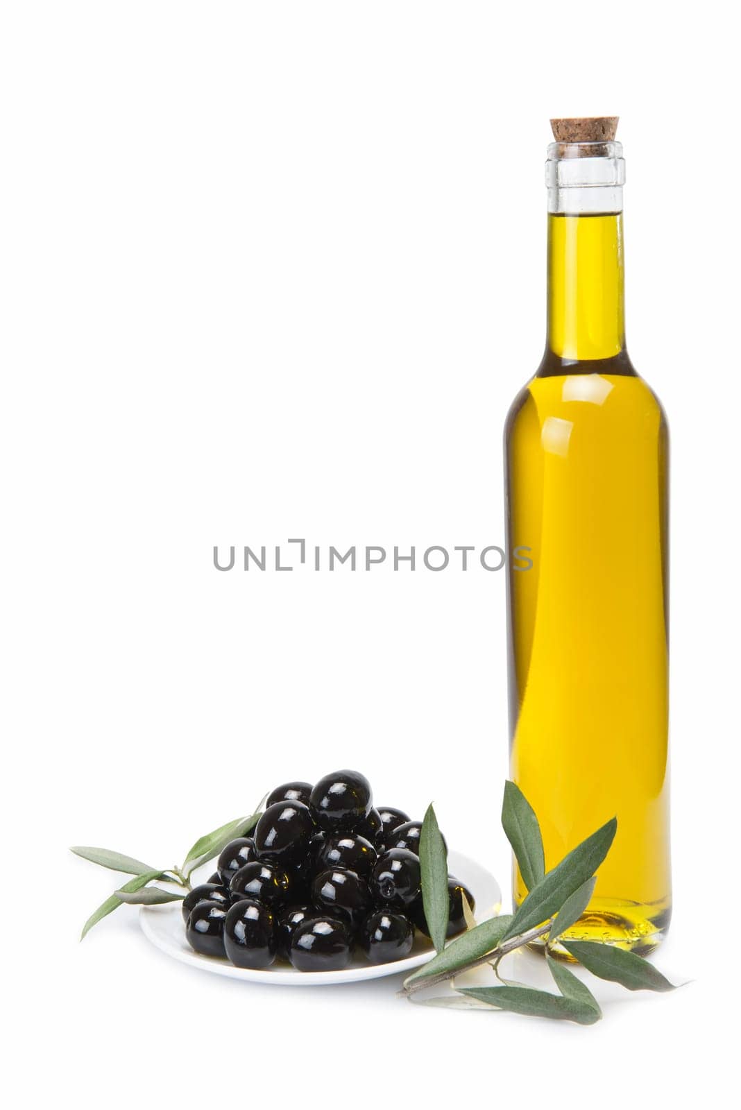 A classical glass bottle of olive oil and a plate with black olives isolated over a white background.