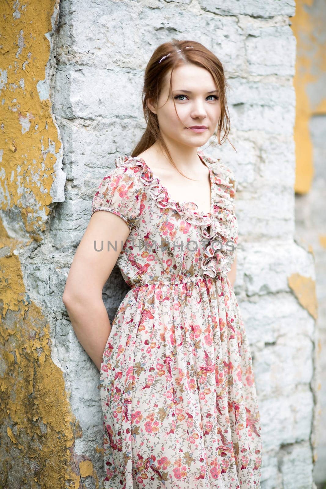 Woman in flowered dress rests on stone wall