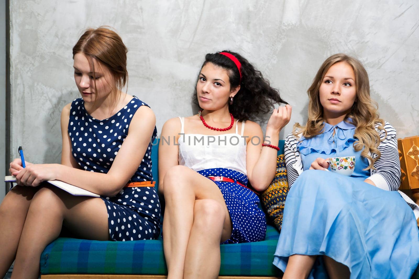 Three womans in different dresses sit on sofa