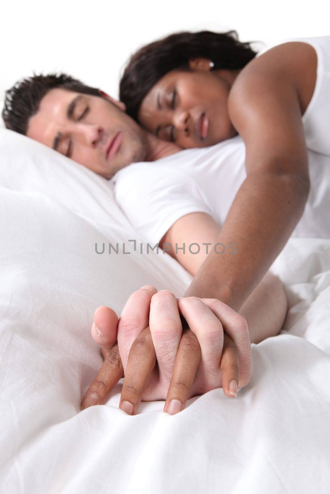 Young couple asleep holding hands in bed