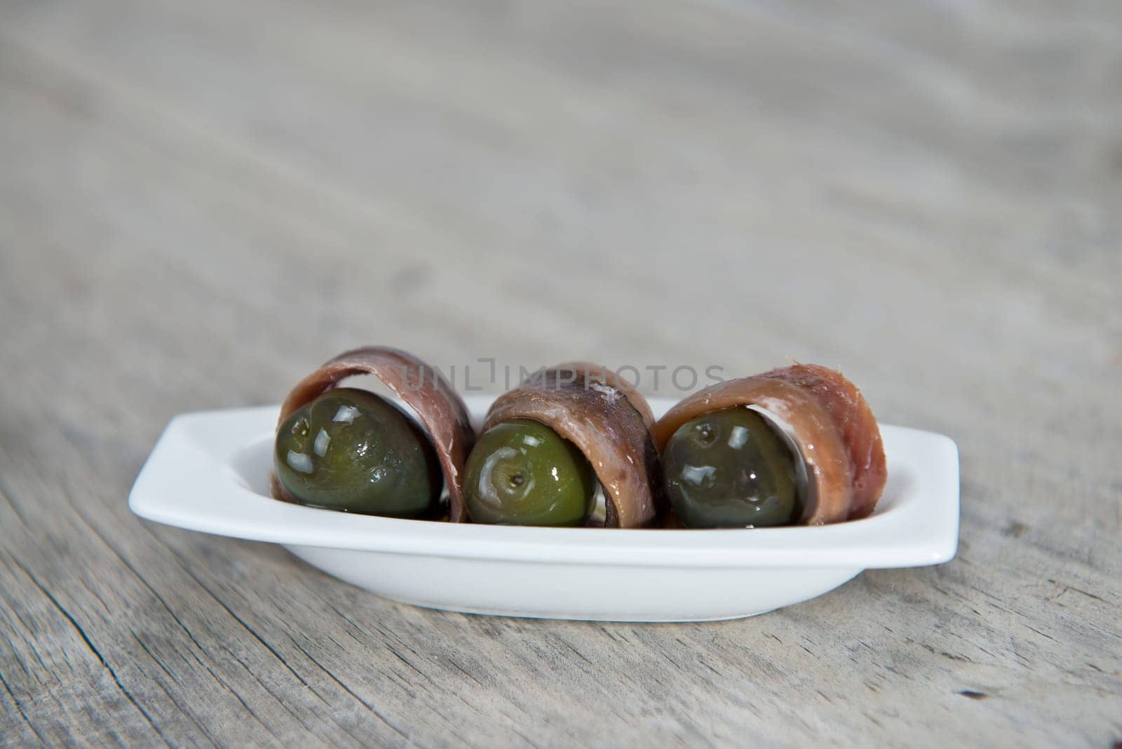 Anchovy appetizer served with green olives in a china spoon on a wooden background