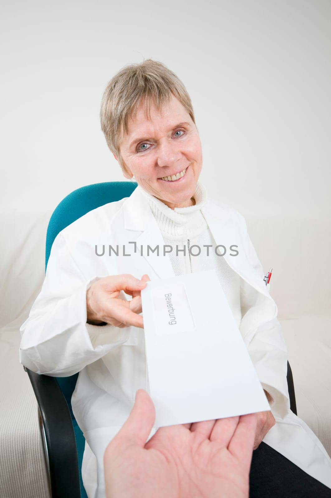 elderly woman sitting on a chair in a white doctor's coat receives an envelope with an application letter from the direction of the camera from one hand