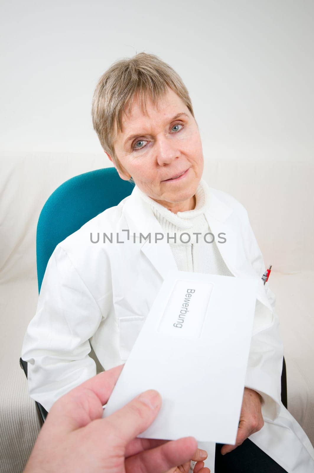 elderly woman sitting on a chair in a white doctor's coat receives an envelope with an application letter from the direction of the camera from one hand