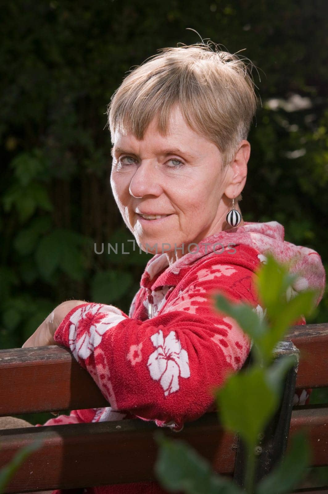 Portrait of an elderly woman on a park bench in summer with her upper body turned backwards over her backrest towards the camera