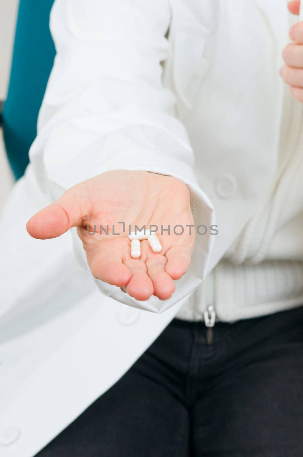 on the hand of an unrecognizable seated woman lie three medicine capsules