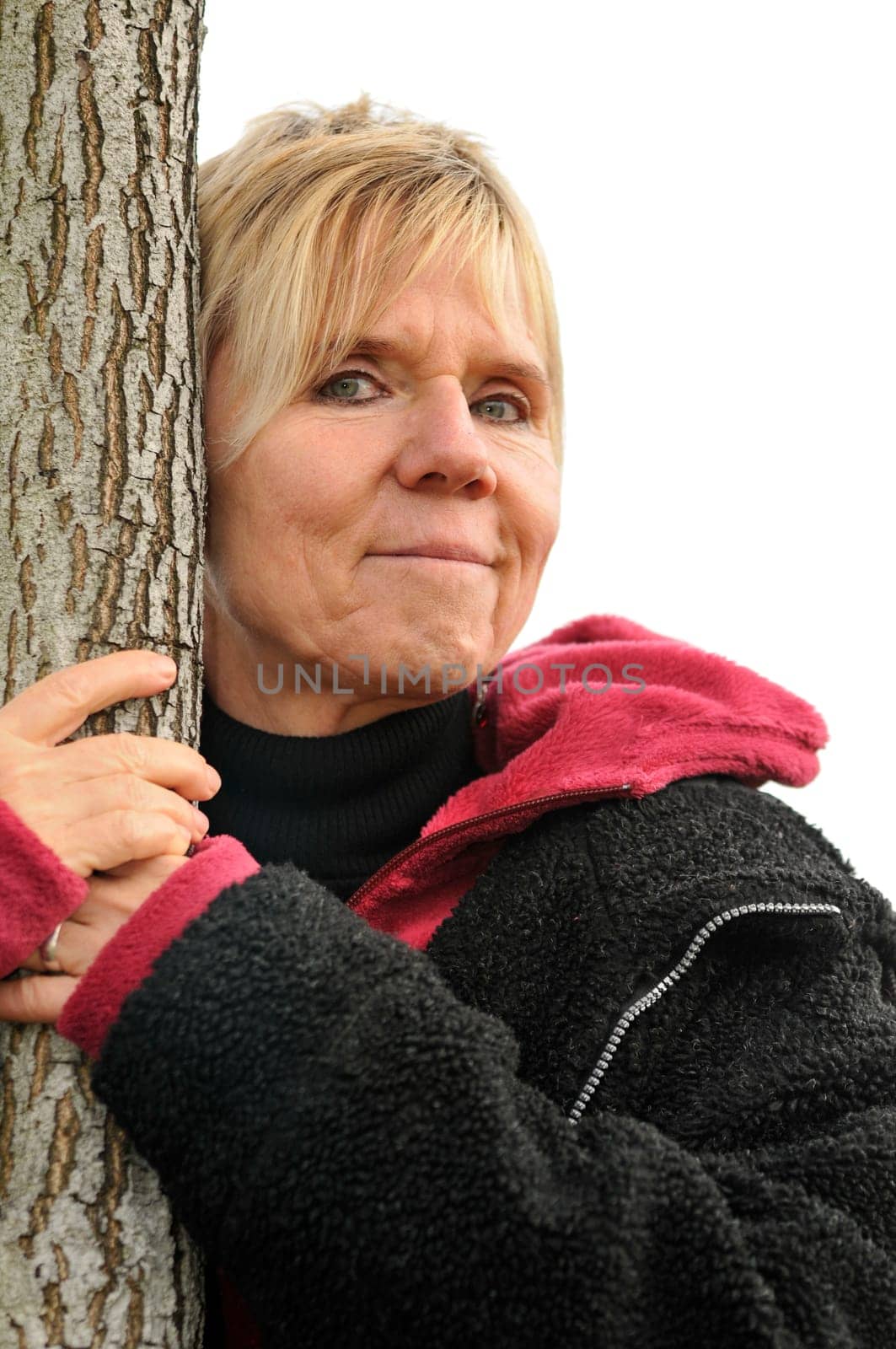 more mature female embraces a slender tree  mature woman is embracing a small tree trunk