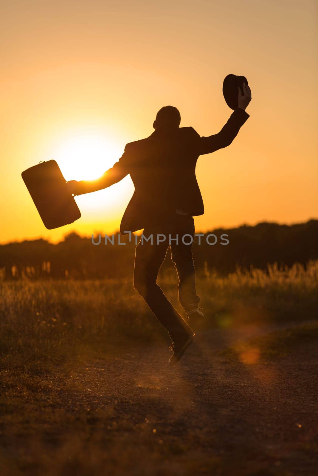 A young man with bag and hat jumps into the sunset with happiness
