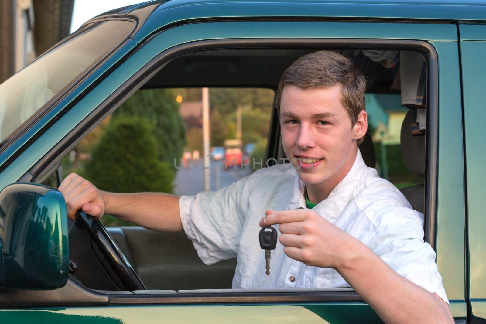 A young man sits in the car and holds up the car keys