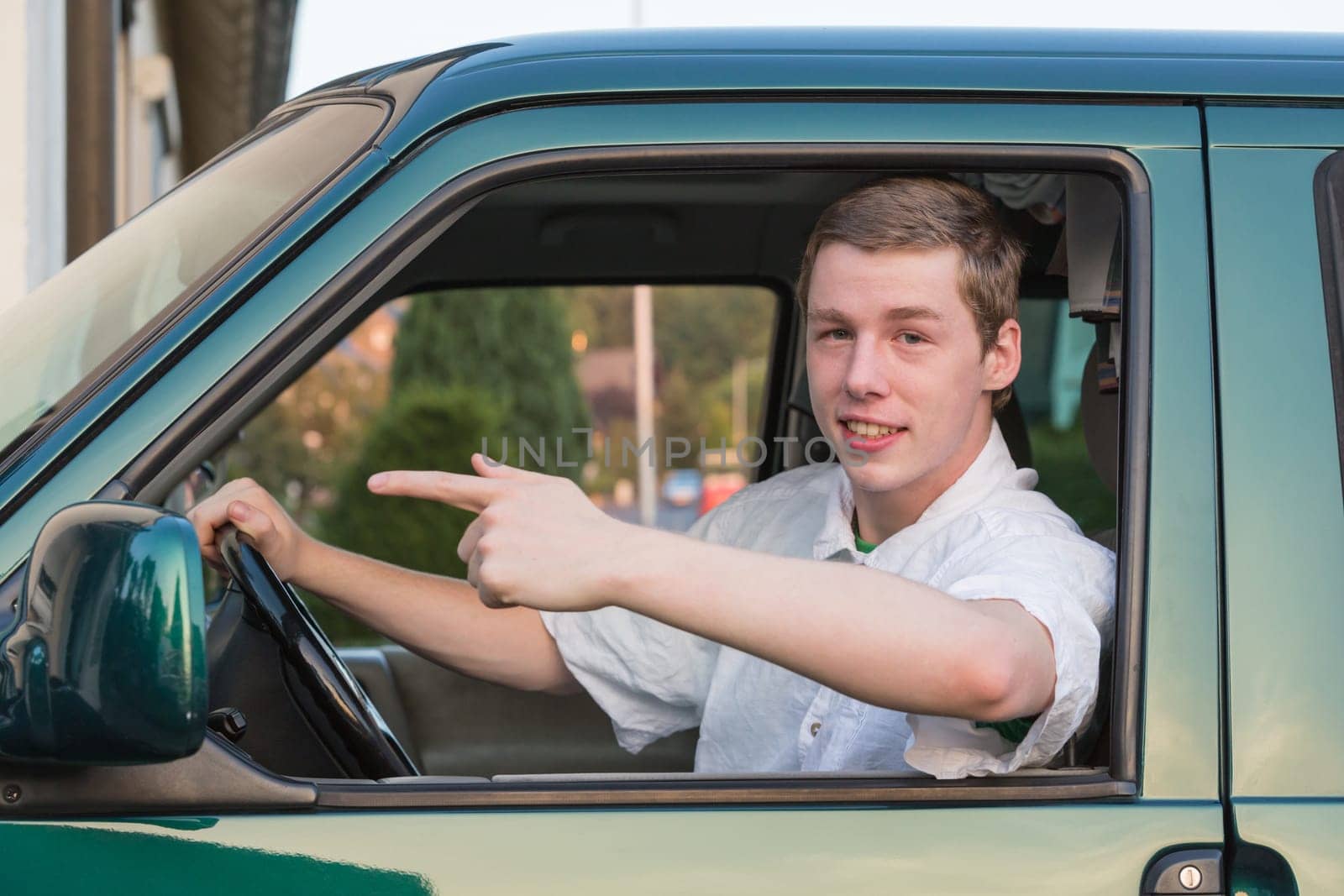 A young man sits in the car and points forward