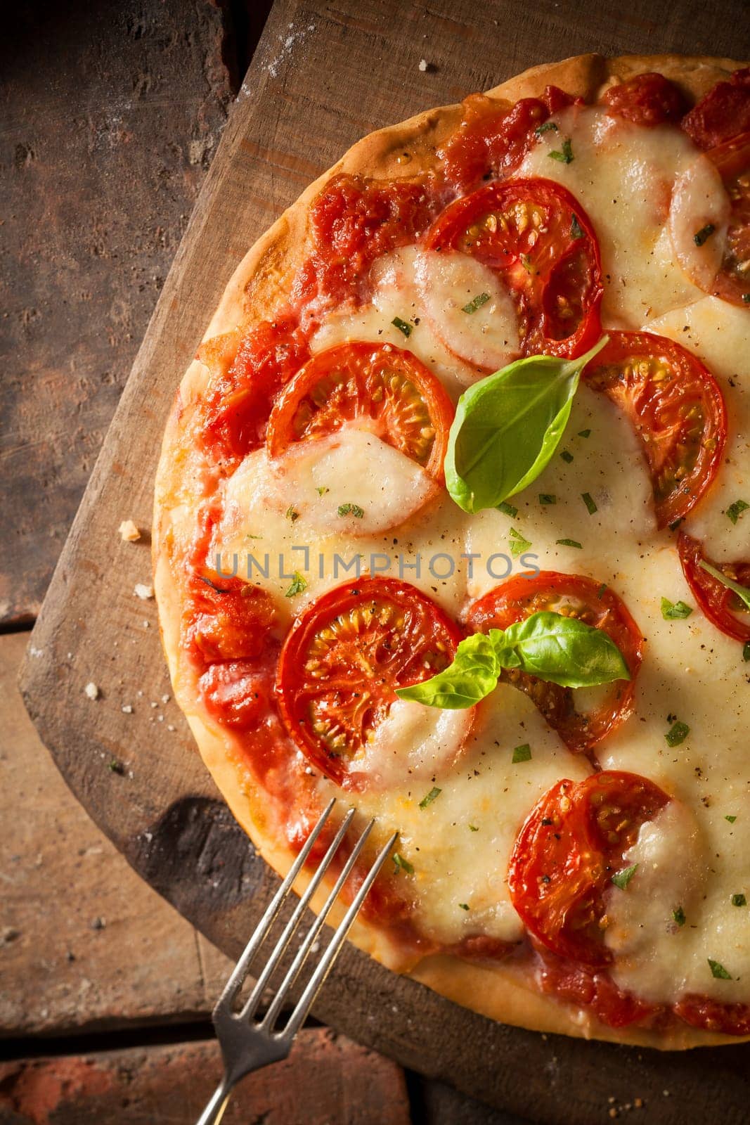 Overhead view of an appetizing tomato pizza with golden melted cheese and basil served on an old wooden board