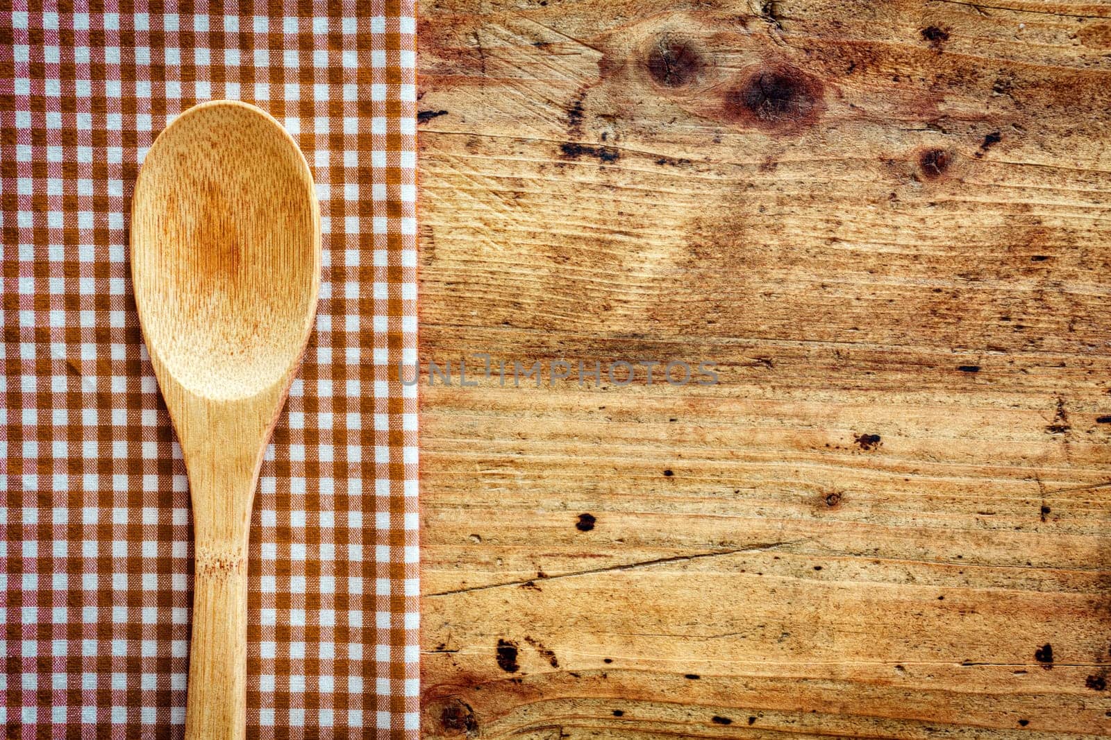 Wooden kitchen spoon on a fresh checkered rustic red and white napkin on a wooden counter with copyspace