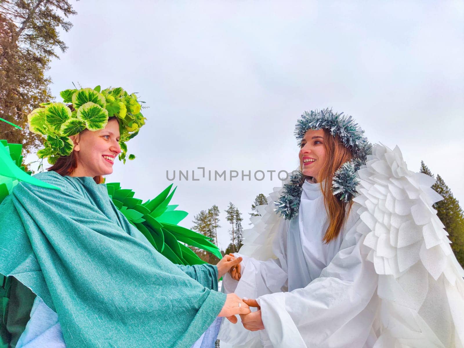 Two girls wear white and green dresses, embodying the seasons of winter and spring, while enjoying a serene moment by the lake.