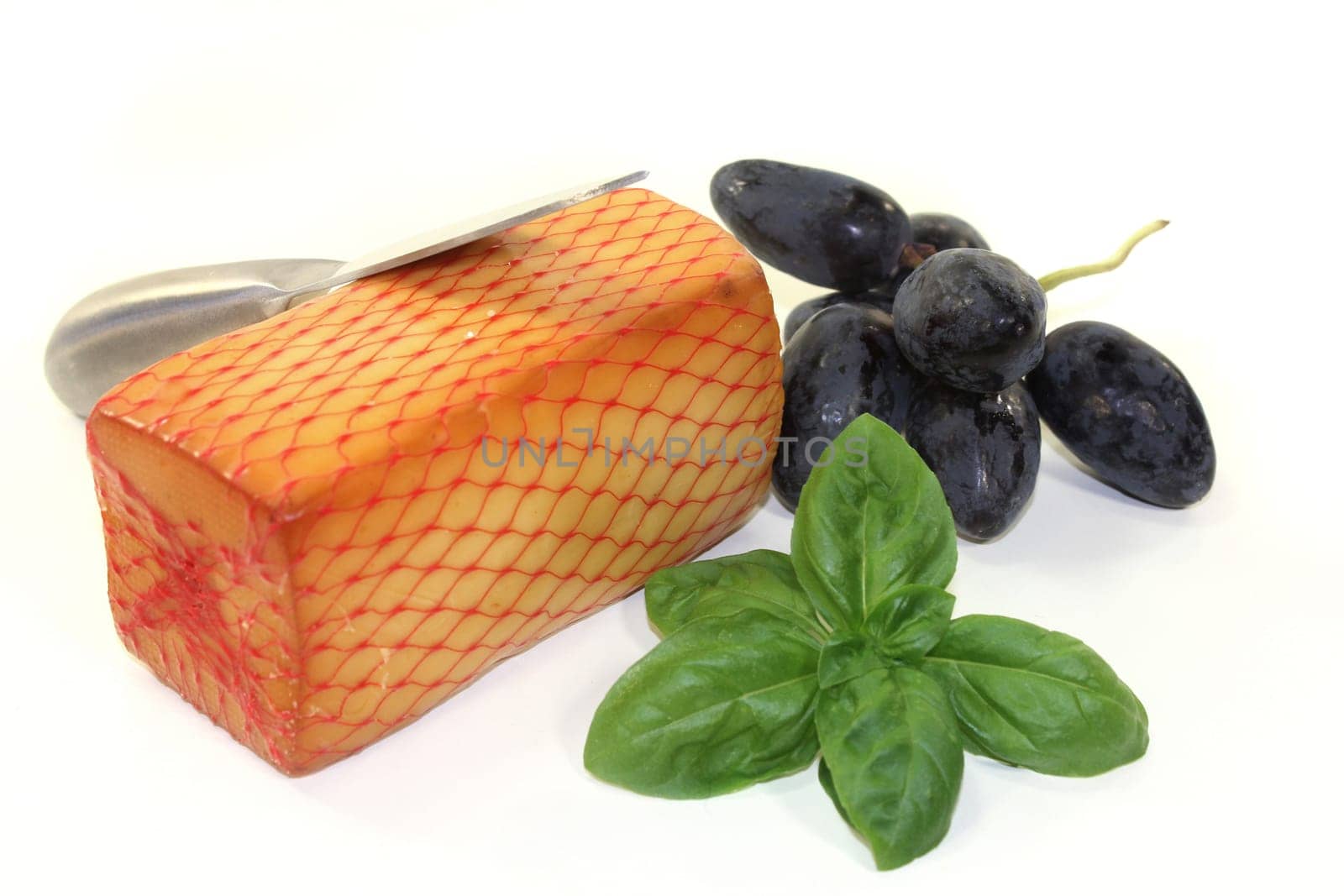 a piece of cheese with cheese knife and basil