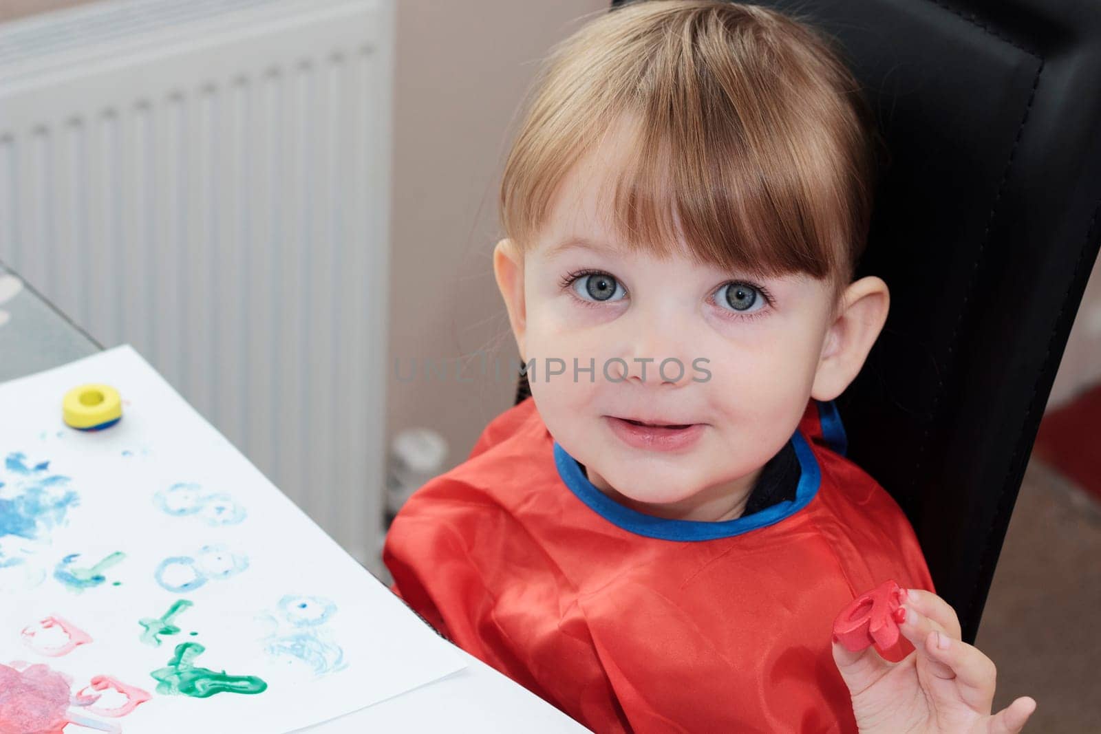 preschool girl painting a picture with foam letters, and looking directly into the camera