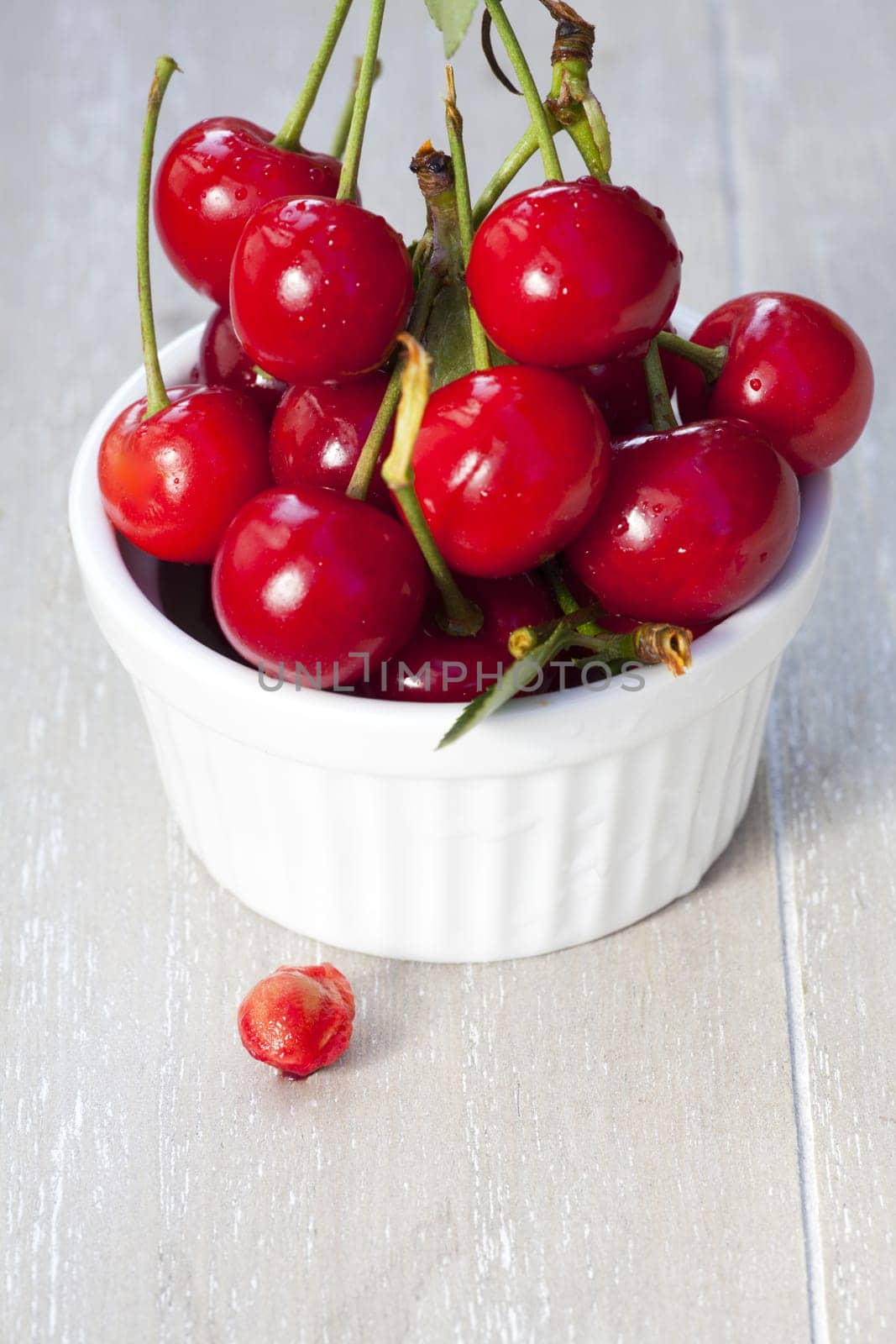 Bowl with cherries and a cherry pit in front of it