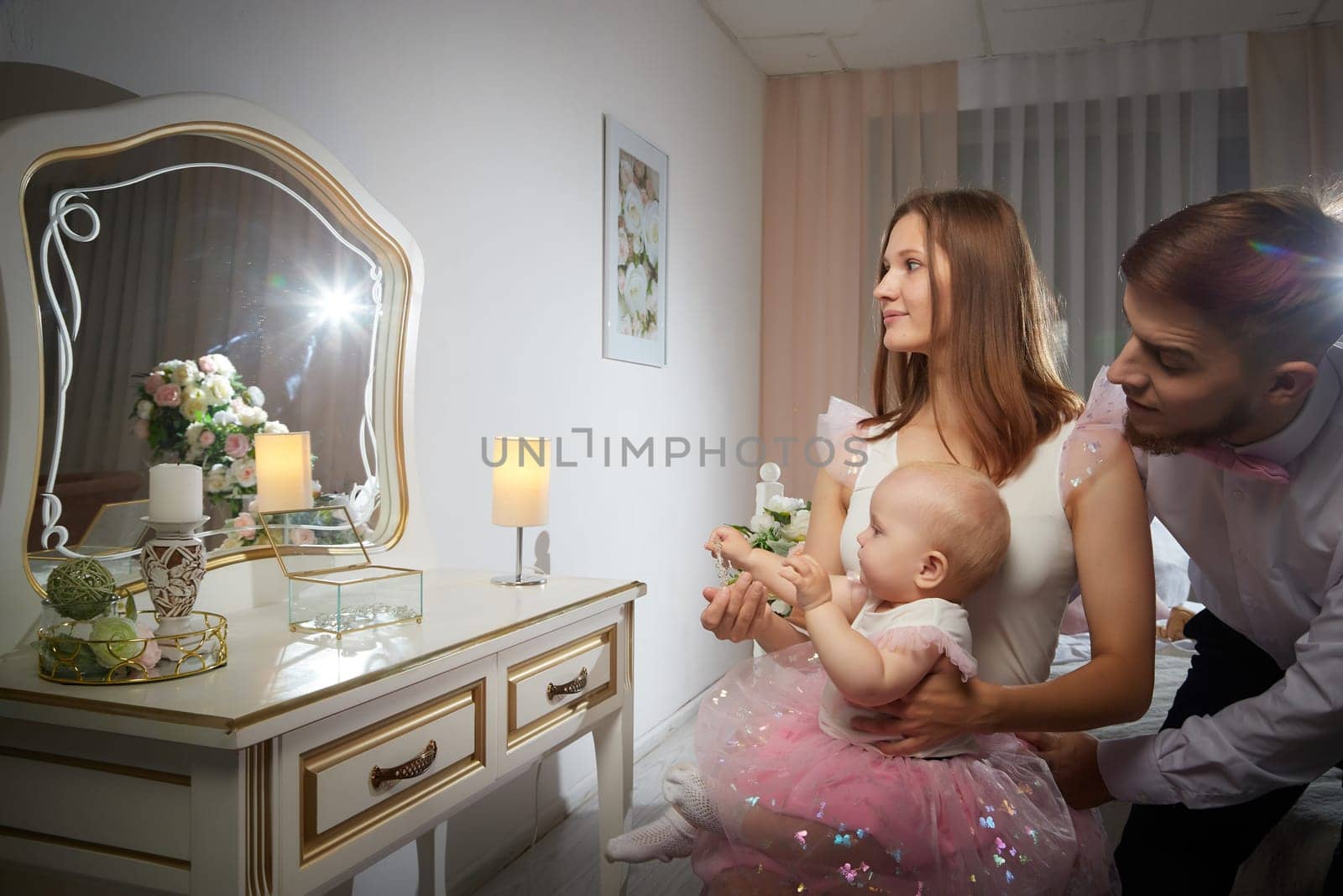 A smiling couple poses with their baby girl at a charming vanity, showcasing joy and affection in a warm and stylish setting.