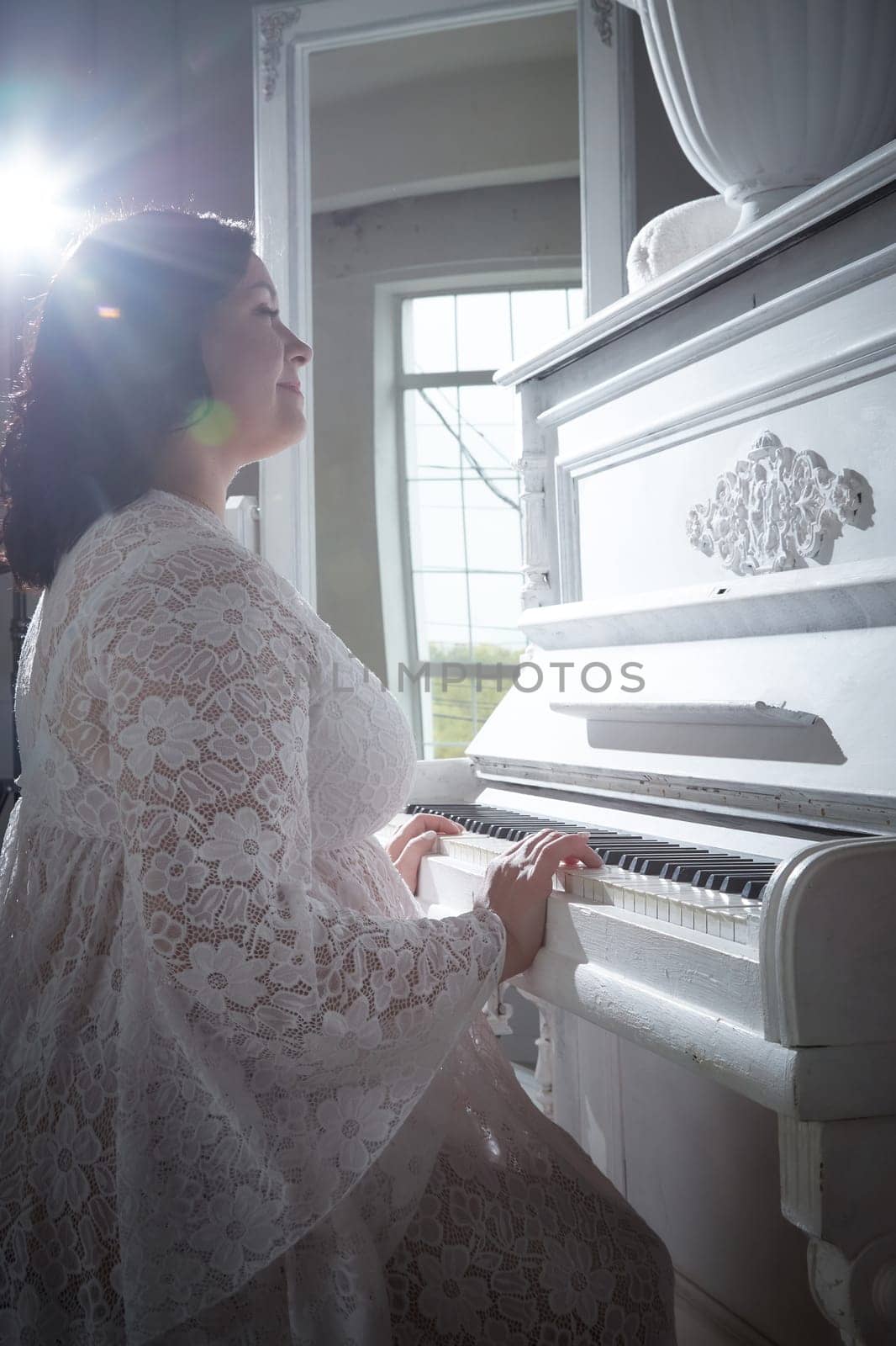 A woman wearing a delicate dress gracefully plays a white piano, illuminated by warm sunlight streaming through a large window.