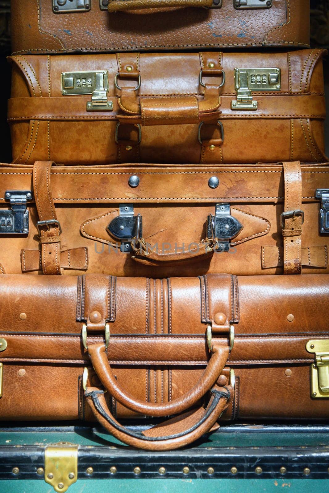 Stack of vintage brown leather suitcases on an old green trunk in a partial close up view conceptual of travel or the Grand Tour