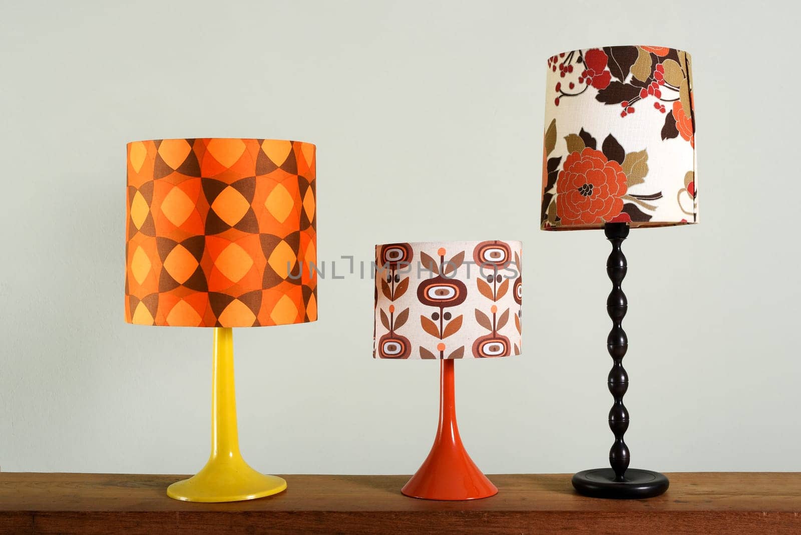 Still Life Collection of Vintage Decorative Lamps - Three Table Lamps with Colorful Bases and Lamp Shades on Wood Table Surface with Plain Background