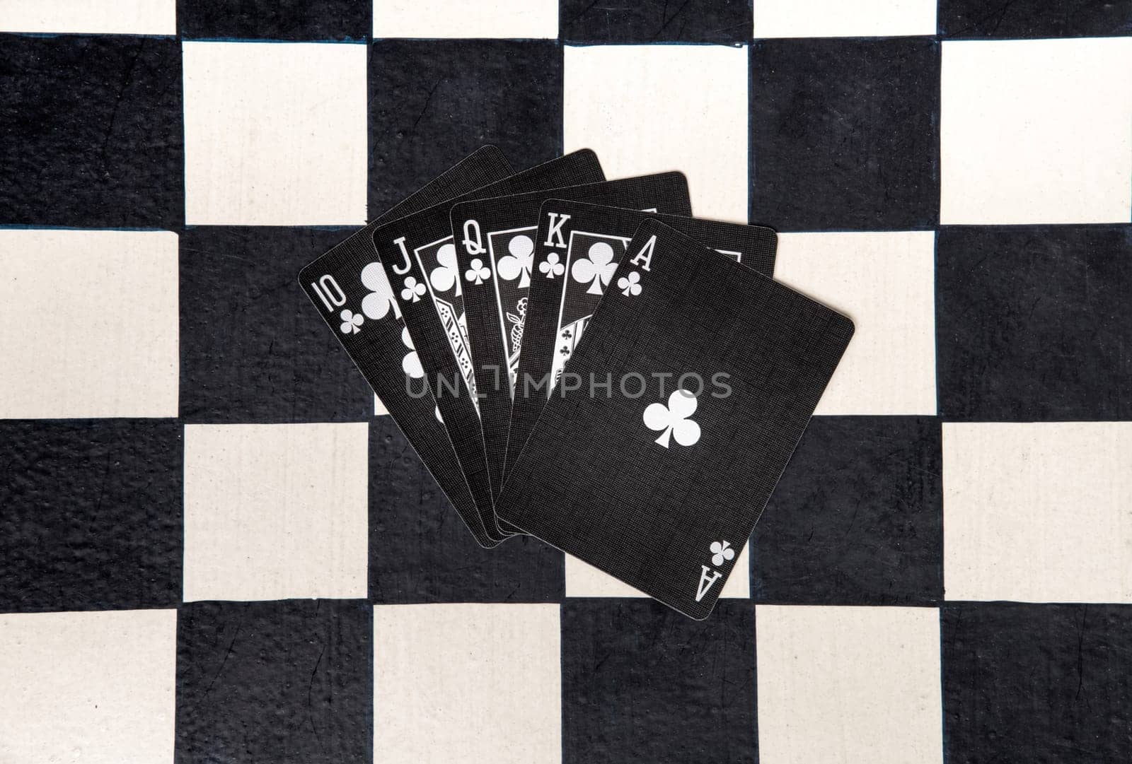 Royal flush or unbeatable winning poker hand in clubs on black cards on a chessboard viewed fanned out from overhead in a flat lay