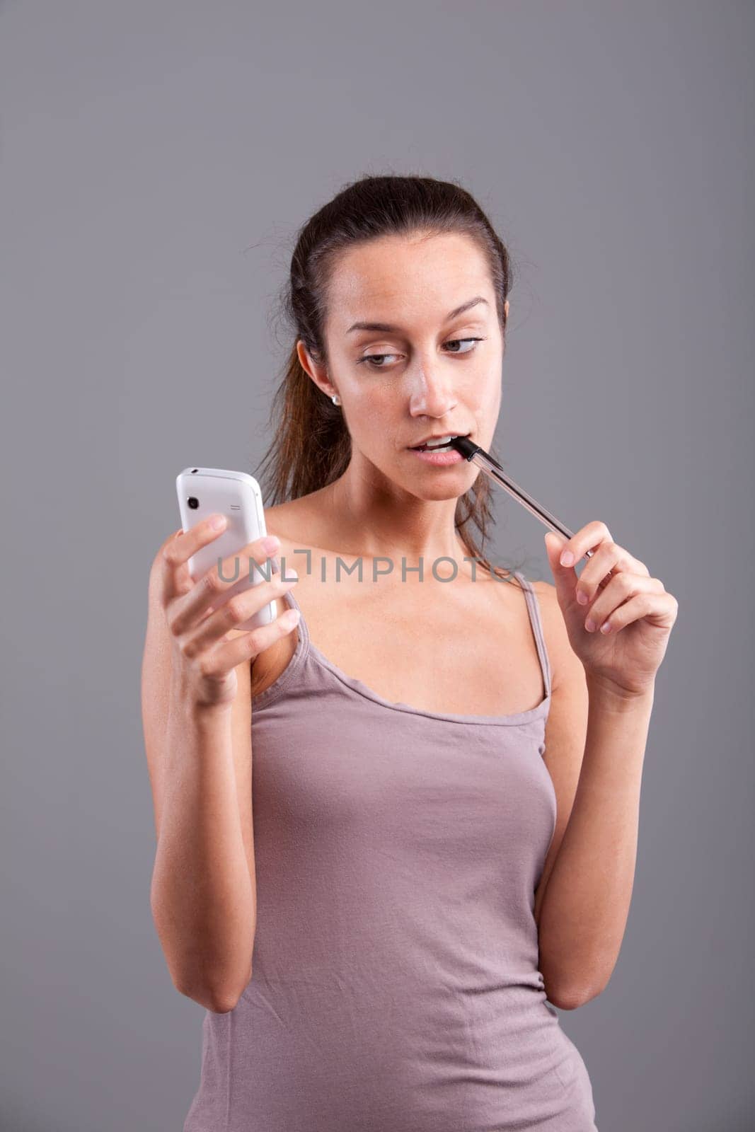 Young woman looking at her smartphone nibbling at her pen