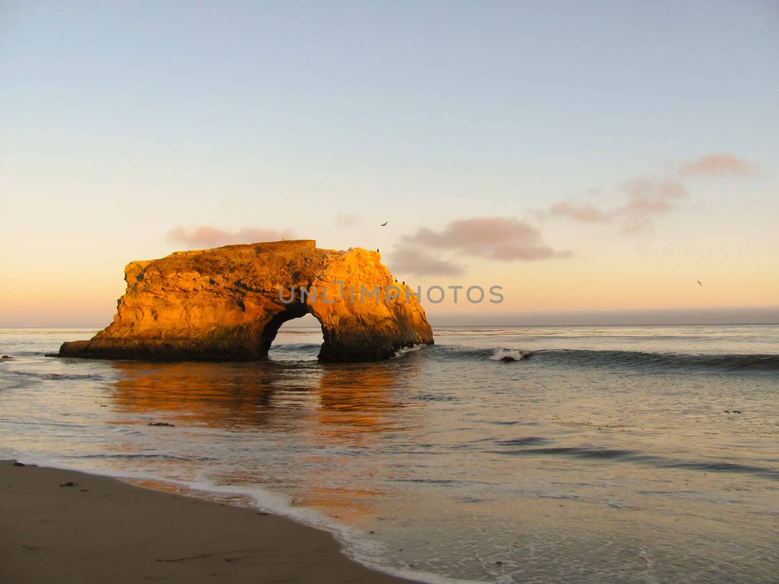 Arch rock formation on ocean beach during sunset
