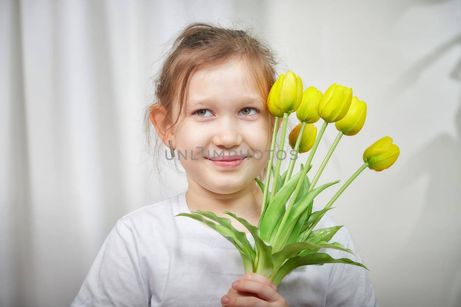 A cheerful girl with a bouquet of yellow tulips enjoys her time indoors, capturing a joyful moment in a cozy setting.