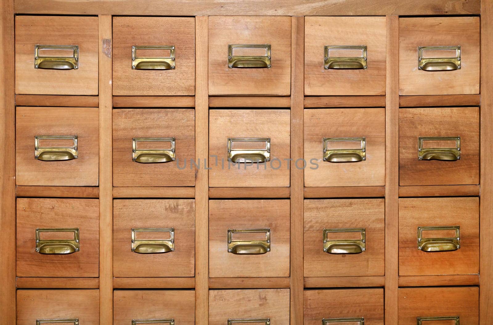 Cabinet with rows of small wooden drawers with brass handles and label holders in a symmetrical full frame background view