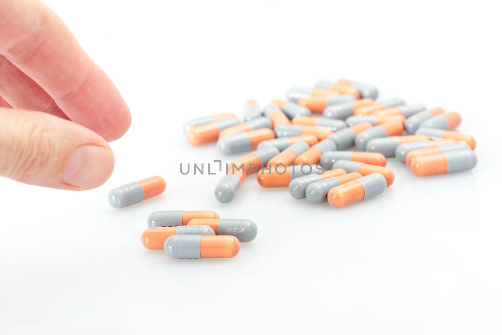 several orange and grey tablets on a flat surface, with fingers reaching to pick one up