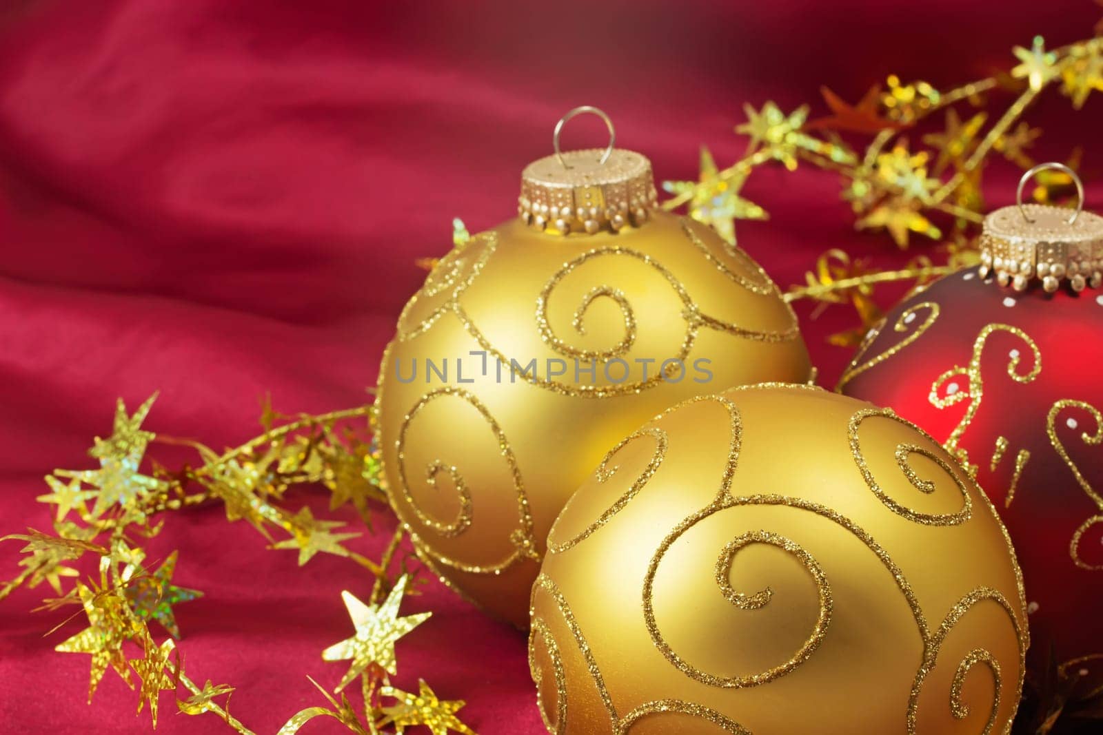 Two golden and one red christmas bulbs with gold chain on a red background