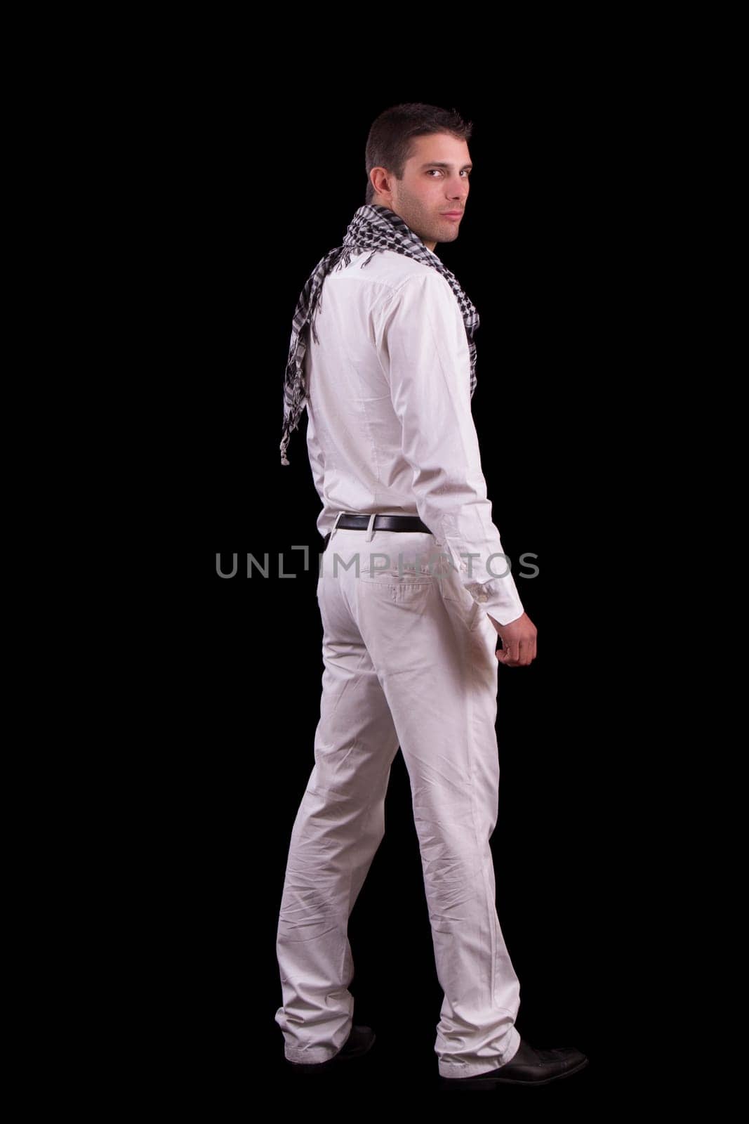 View of a young urban styled fashioned man standing isolated on a black background.